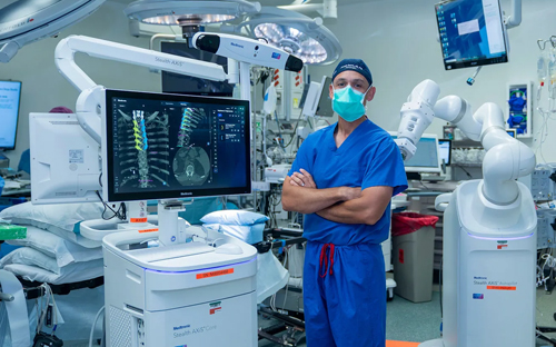 Joseph Osorio, MD, PhD, neurosurgeon at UC San Diego Health, stands beside the new AI-powered robotic spine surgery system in an operating room at Jacobs Medical Center. Photo credit: Leslie Aquinde, UC San Diego Health