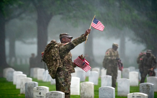 Soldier putting flags on graves at Arlington National Cemetery waves to someone off camera 